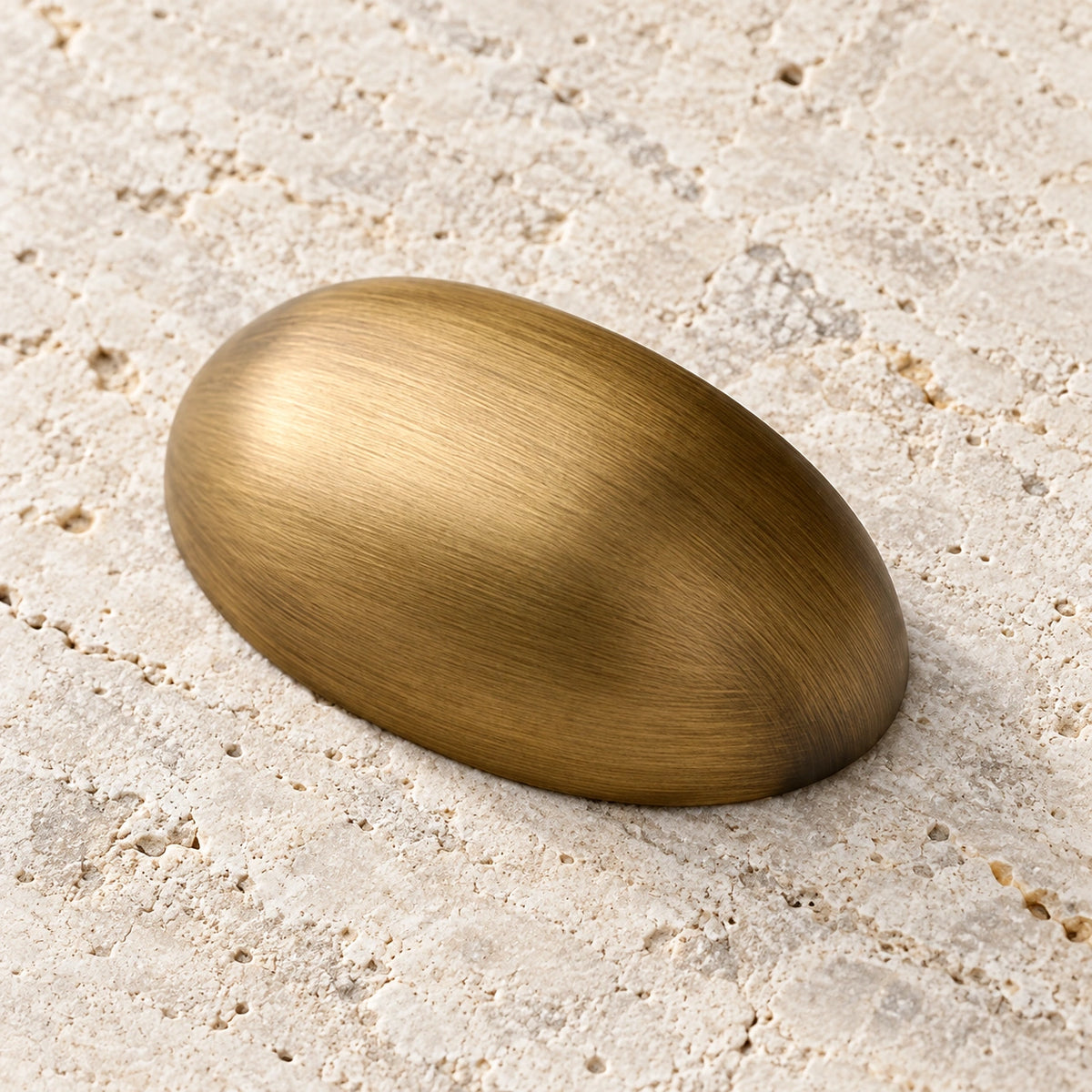 Antique brass oval shell cabinet cup pull on pale limestone