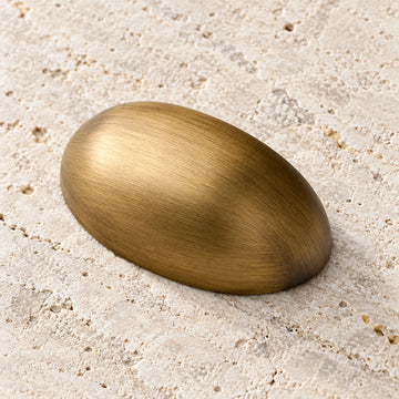 Antique brass oval shell cabinet cup pull on pale limestone