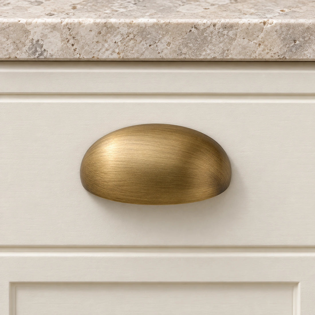 Antique brass oval shell cabinet cup pull on pale limestone