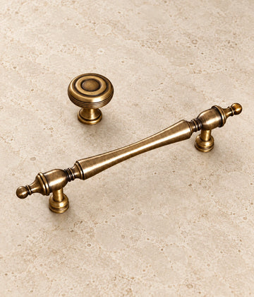 Antique Brass Slender Finial Pulls & Grooved Knobs on warm ivory limestone