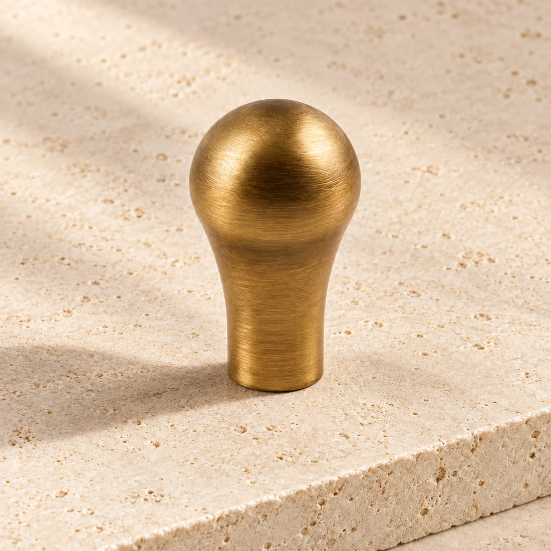 antique brass slim cabinet knob on pale limestone.
