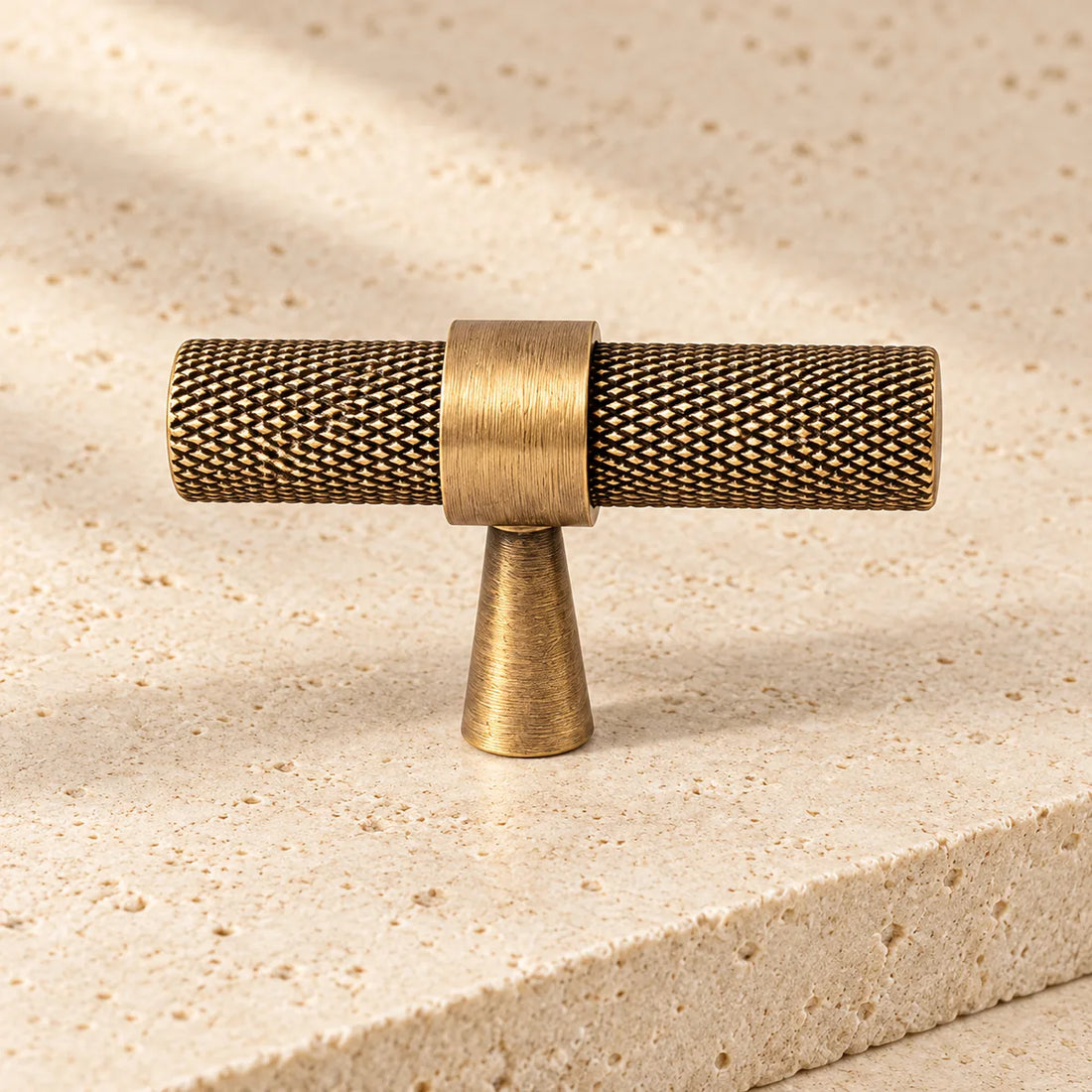 antique brass slim knurled t bar cabinet knob on pale limestone.