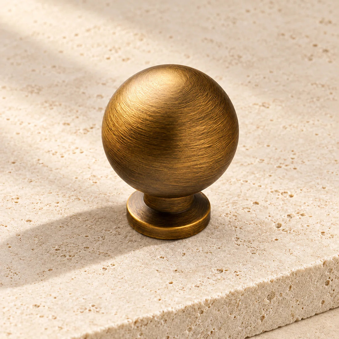 antique brass smooth ball cabinet knob on pale limestone.