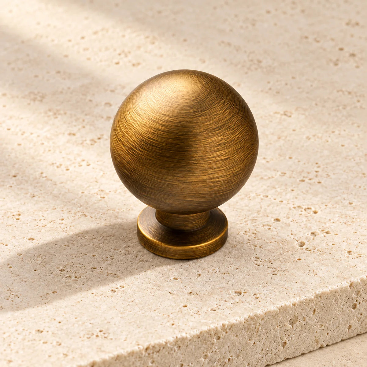 antique brass smooth ball cabinet knob on pale limestone.