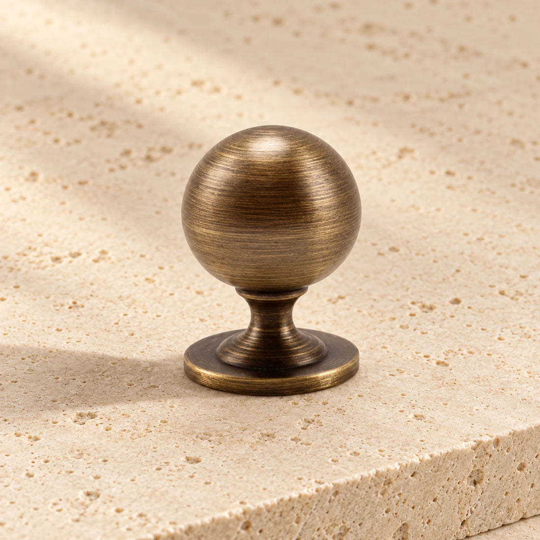 antique brass spindle ball cabinet knob on pale limestone.