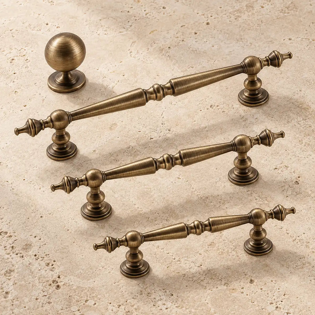 Antique brass spindle cabinet pulls and ball knob arranged on warm limestone