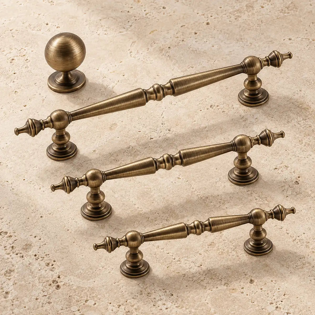 Antique brass spindle cabinet pulls and ball knob arranged on warm limestone