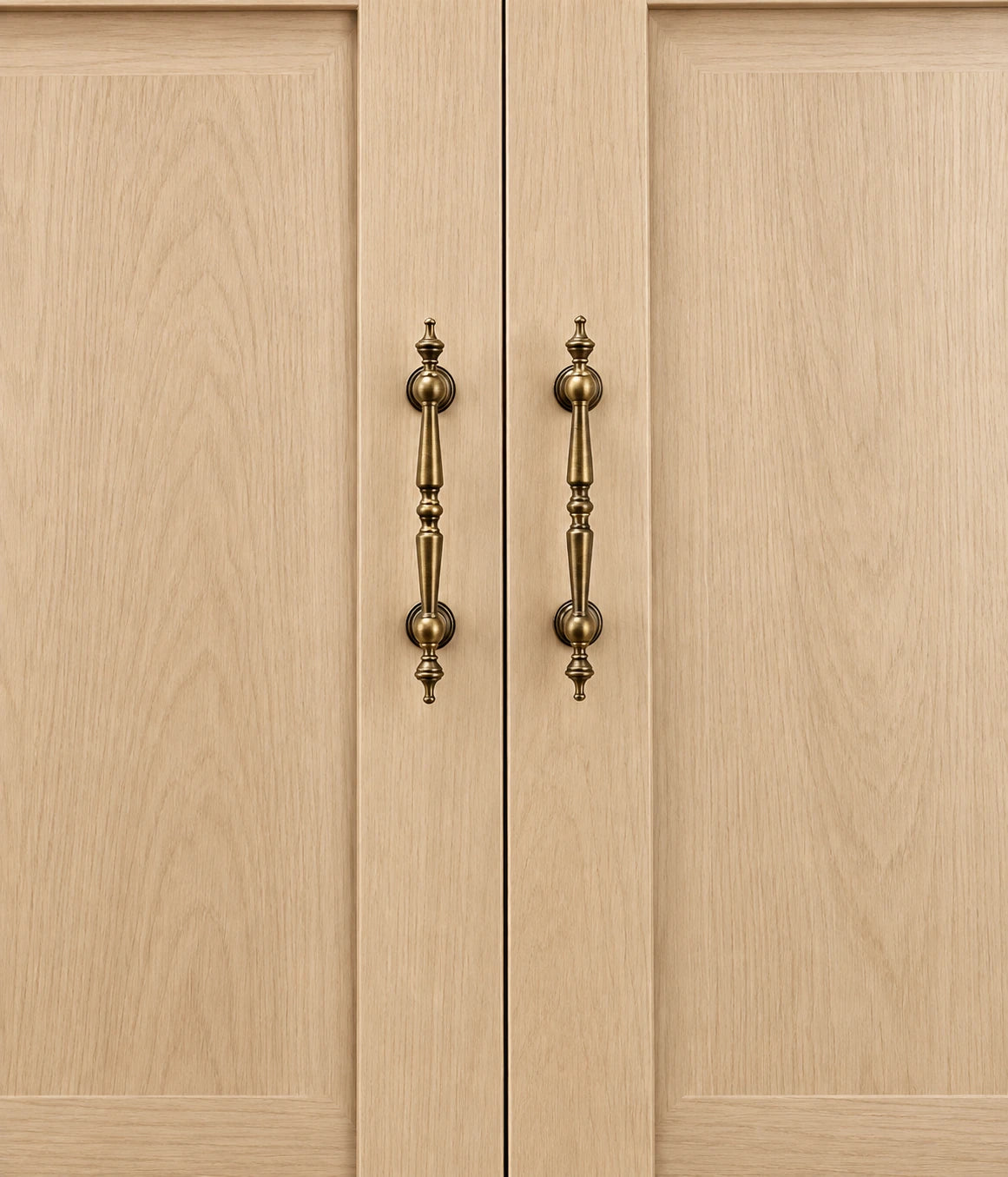 Antique brass spindle cabinet pulls mounted vertically on oak cabinet doors