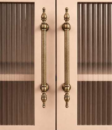 Decorative brass spire-finial cabinet pulls installed vertically on ribbed-glass doors