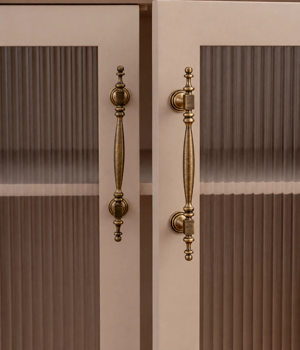 Antique brass square-collar cabinet pulls installed vertically on cream doors with ribbed glass