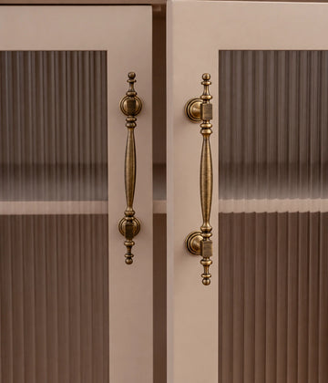 Antique brass square-collar cabinet pulls installed vertically on cream doors with ribbed glass