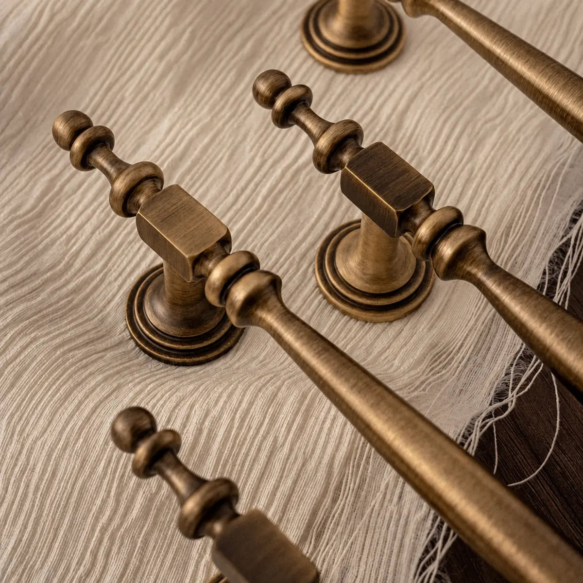 Antique brass square collars, round bases and ringed finials on textured cream fabric