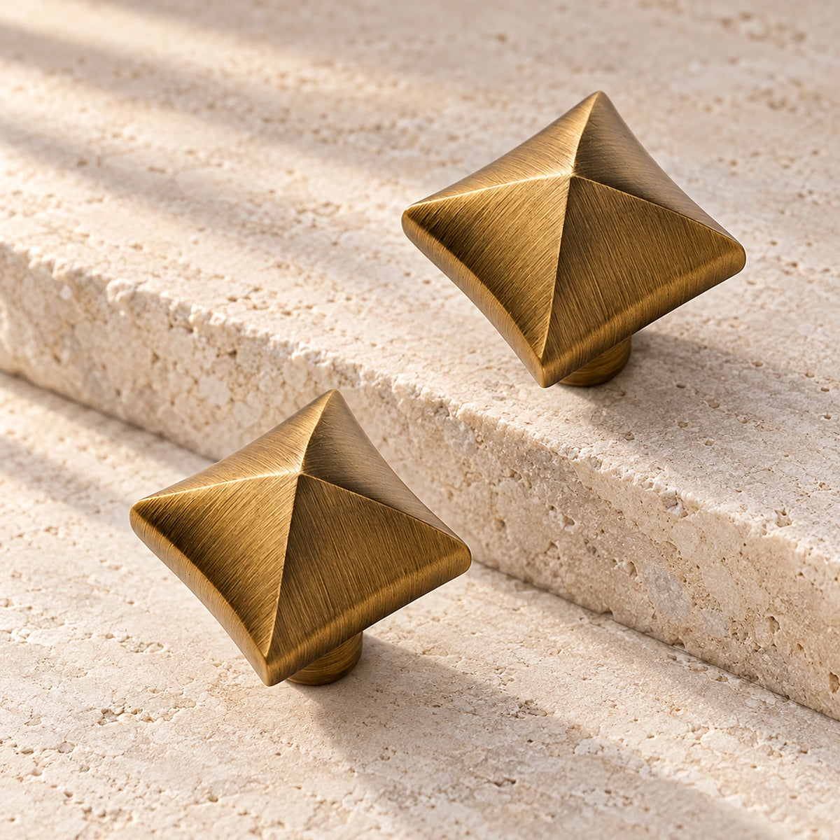 Antique brushed brass square pyramid cabinet knobs on pale limestone