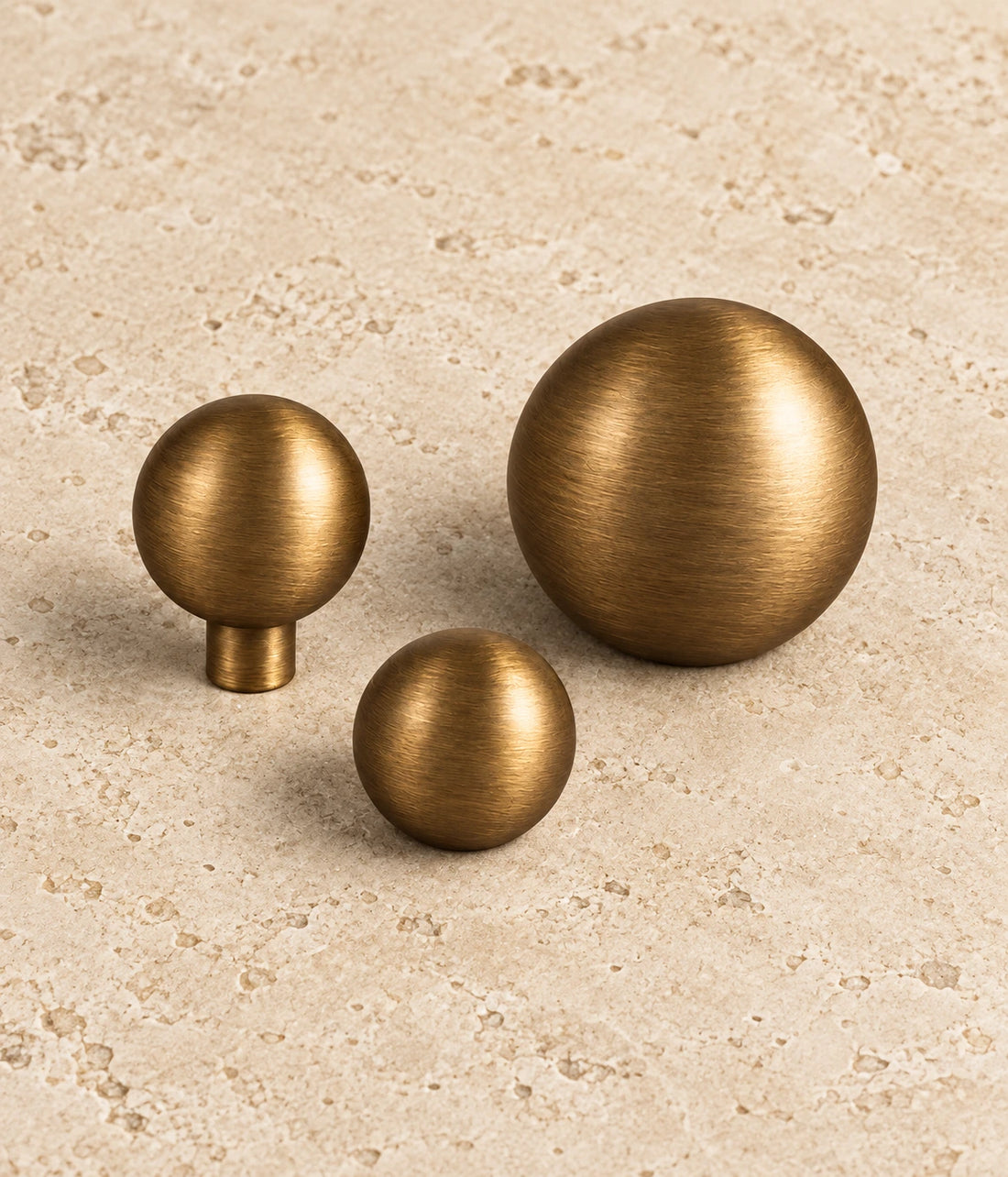 Antique Brass Stemless & Slim-Stem Ball Cabinet Knobs on warm limestone