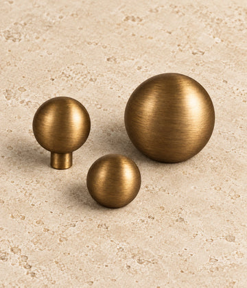 Antique Brass Stemless & Slim-Stem Ball Cabinet Knobs on warm limestone