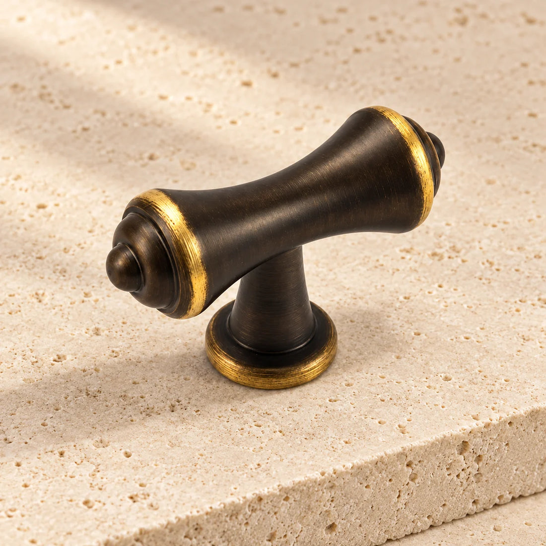 antique brass tapered finial t bar cabinet knob on pale limestone.