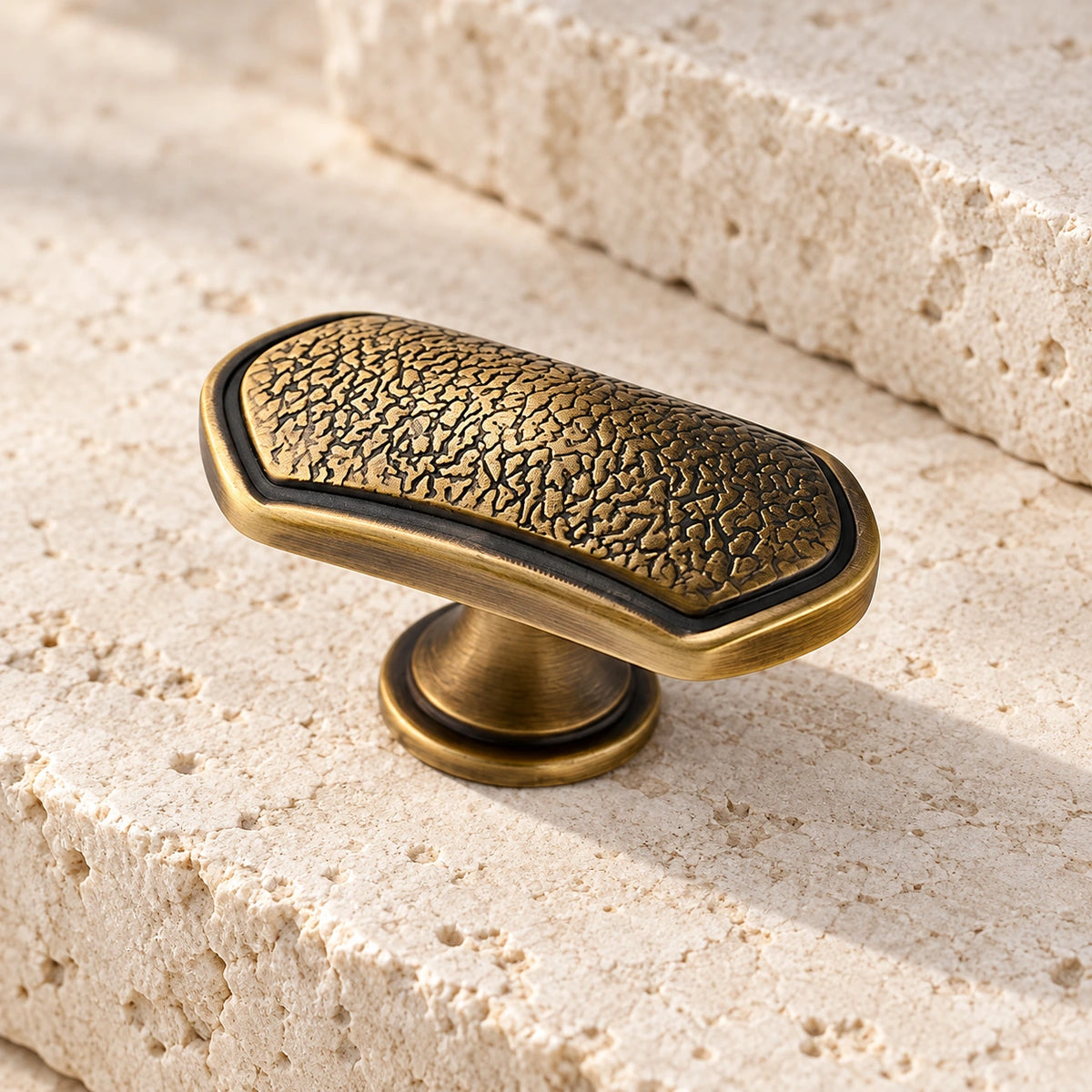 Antique brass textured oblong T-knob with smooth border on pale limestone