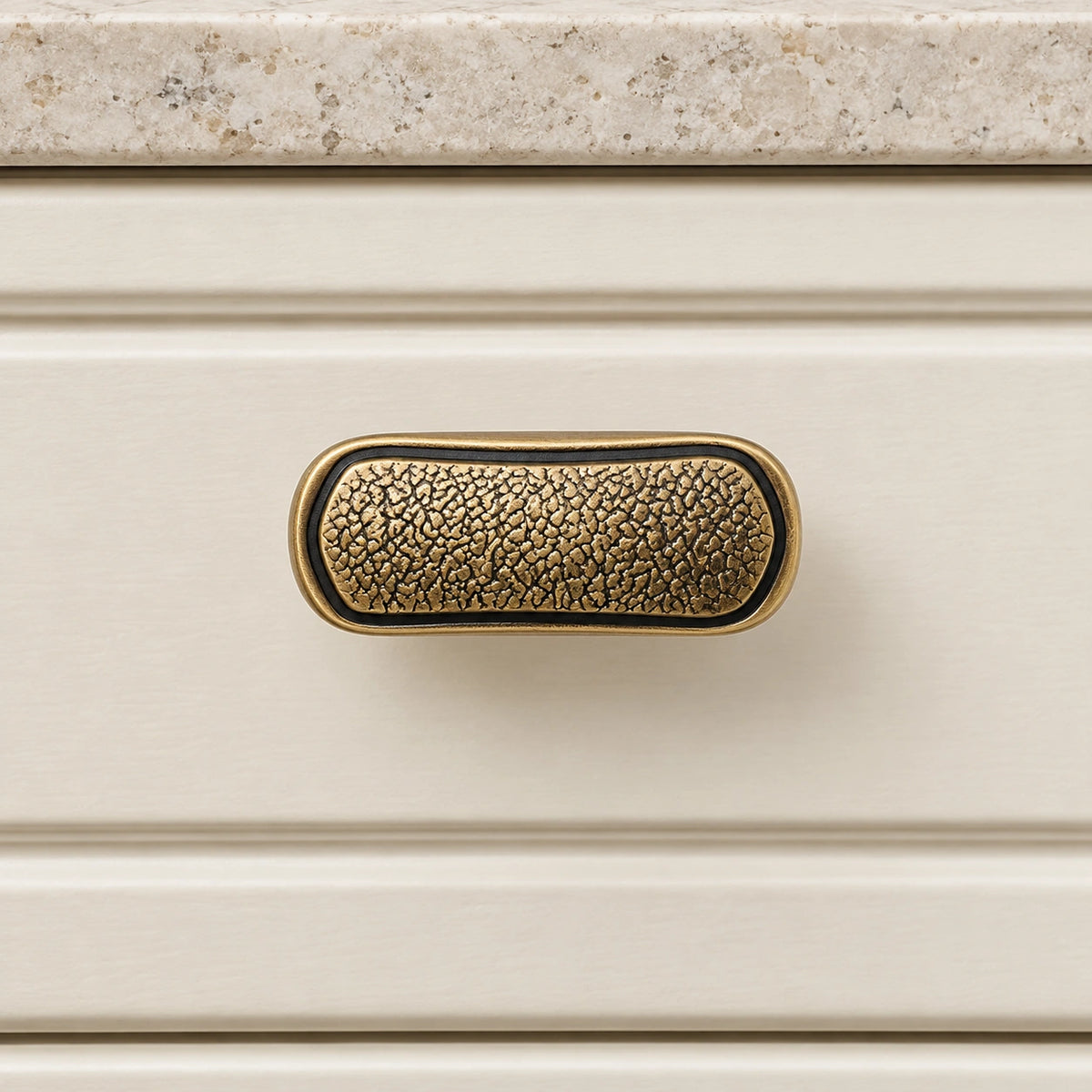 Textured oblong brass T-knob mounted horizontally on an ivory cabinet drawer