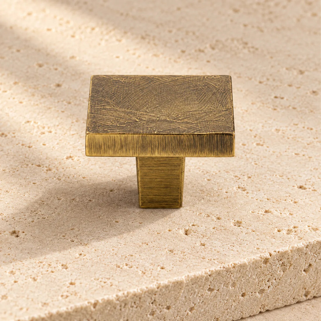 antique brass textured square cabinet knob on pale limestone.