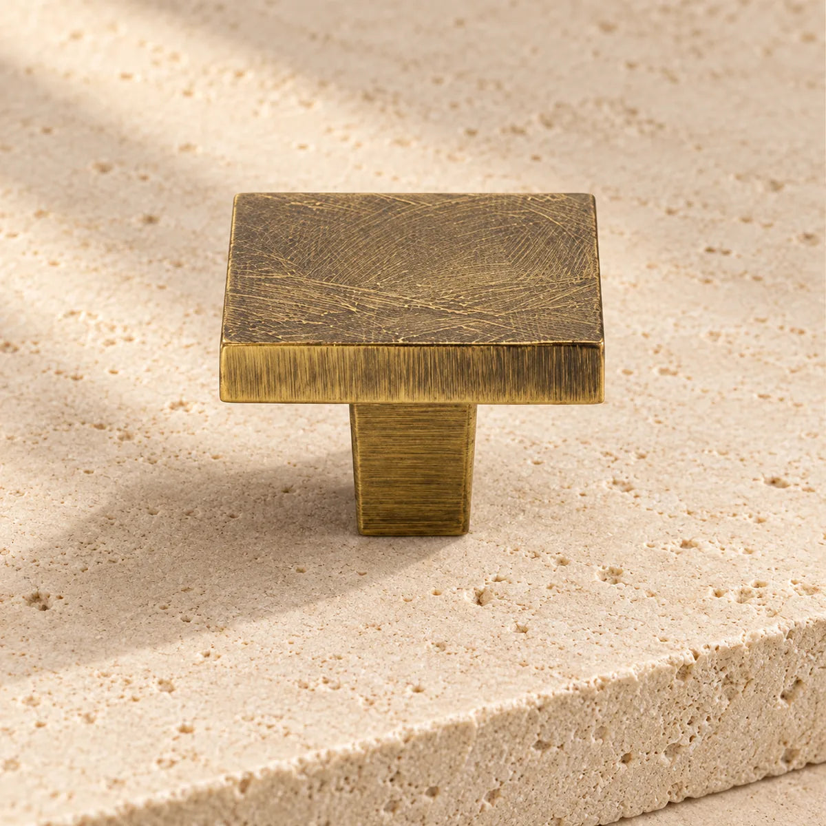 antique brass textured square cabinet knob on pale limestone.