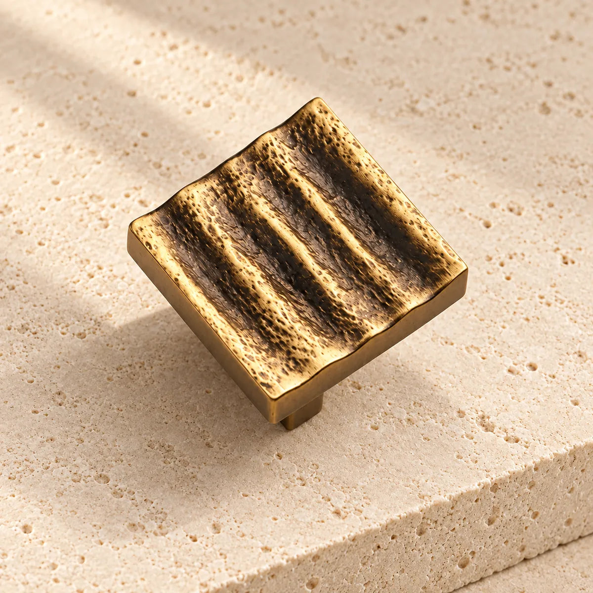 antique brass textured wave square cabinet knob on pale limestone.