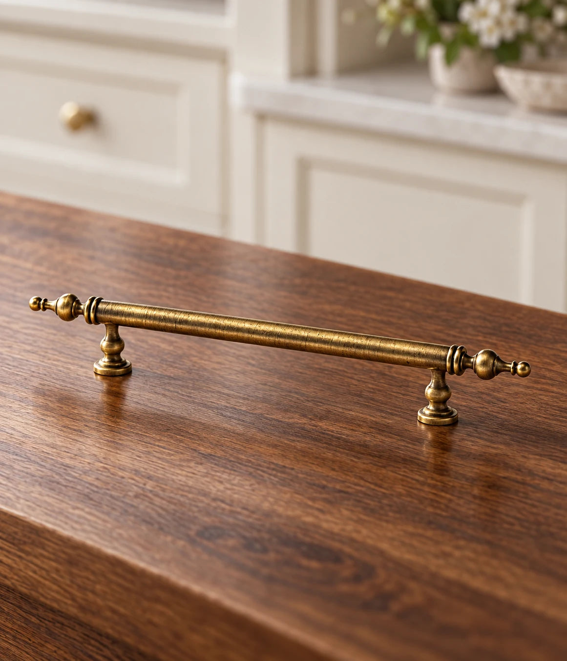 Antique brass turned-post finial cabinet pull resting on walnut beside ivory cabinetry