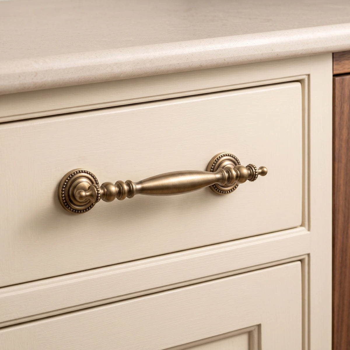 Antique brass urn-end cabinet pull installed on a cream drawer