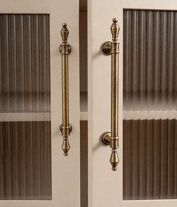 Antique brass urn-finial cabinet pulls installed vertically on fluted-glass cabinet doors