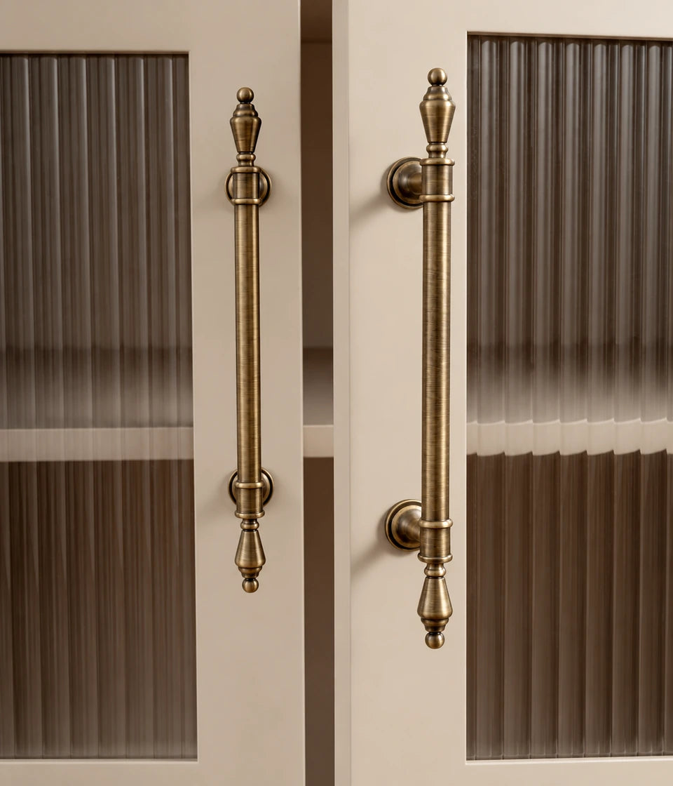 Antique brass urn-finial cabinet pulls installed vertically on fluted-glass cabinet doors