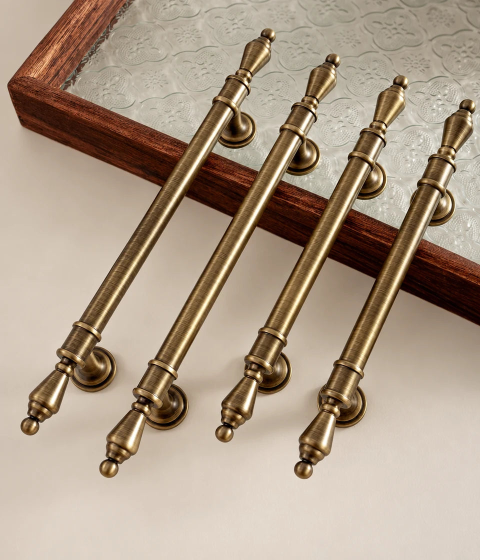 Four antique brass urn-finial cabinet pulls arranged beside a wood and glass tray