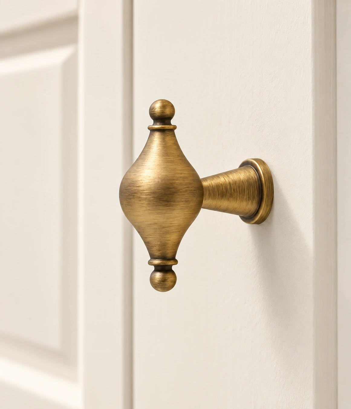 Antique brass spindle T-knob with ball finials mounted on an ivory cabinet door