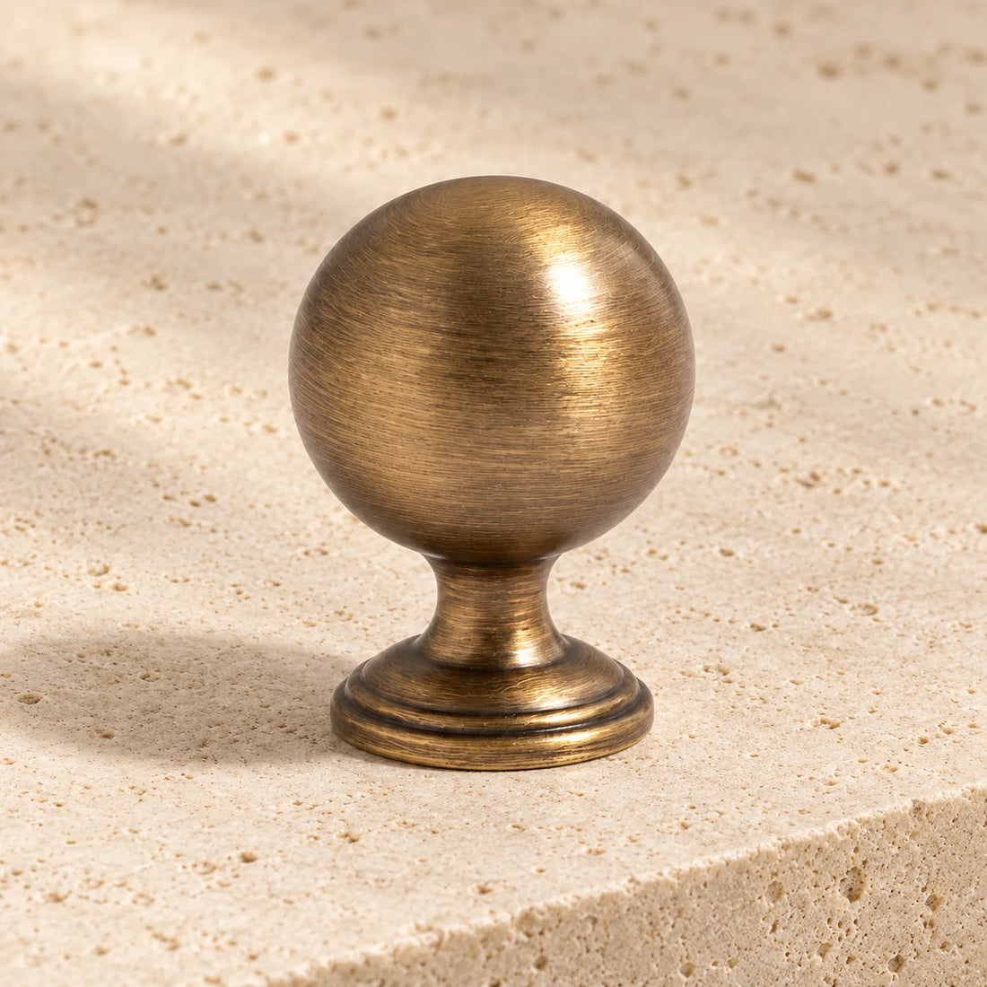 antique brass waisted ball cabinet knob on pale limestone.