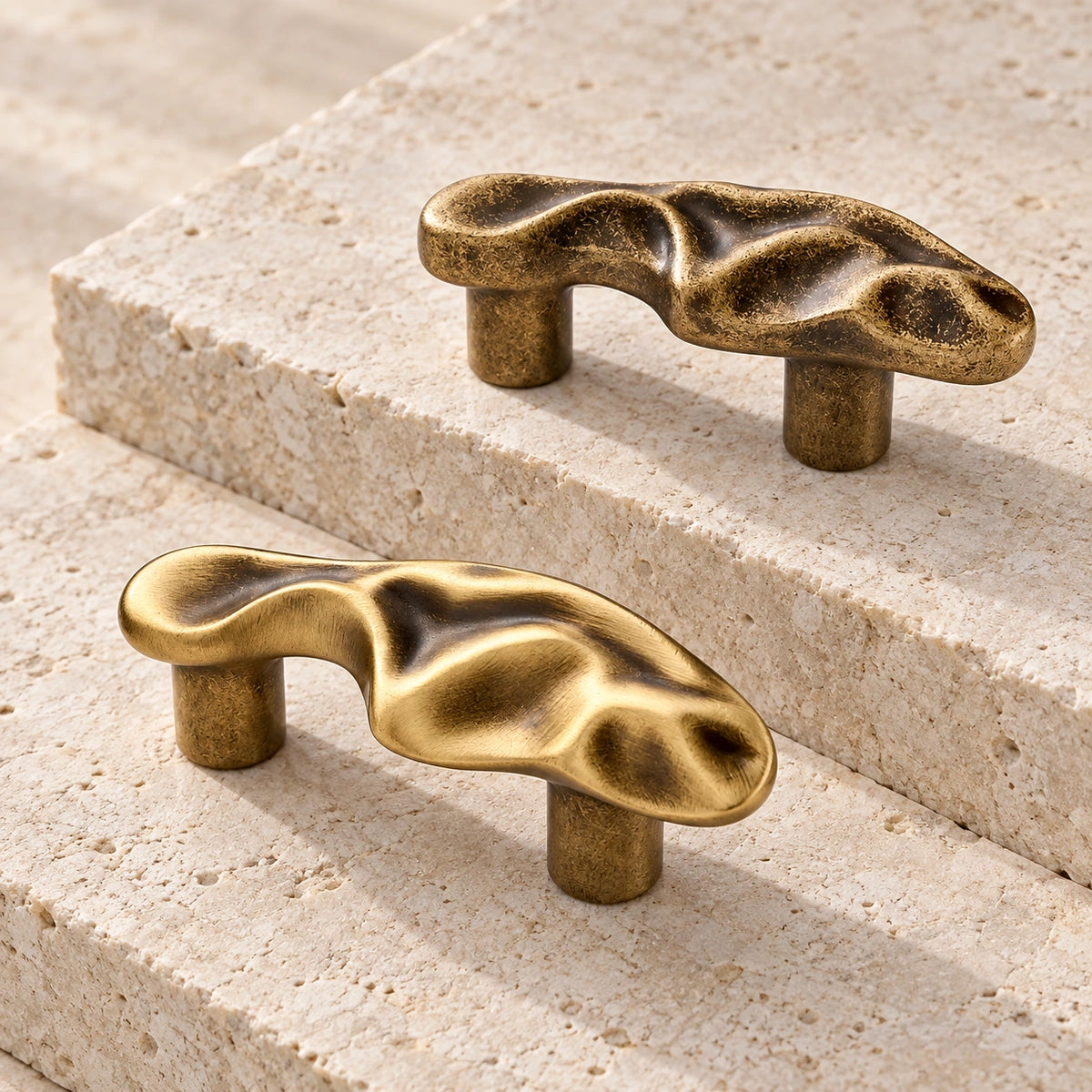 Aged and brushed antique brass sculptural wave cabinet pulls on pale limestone