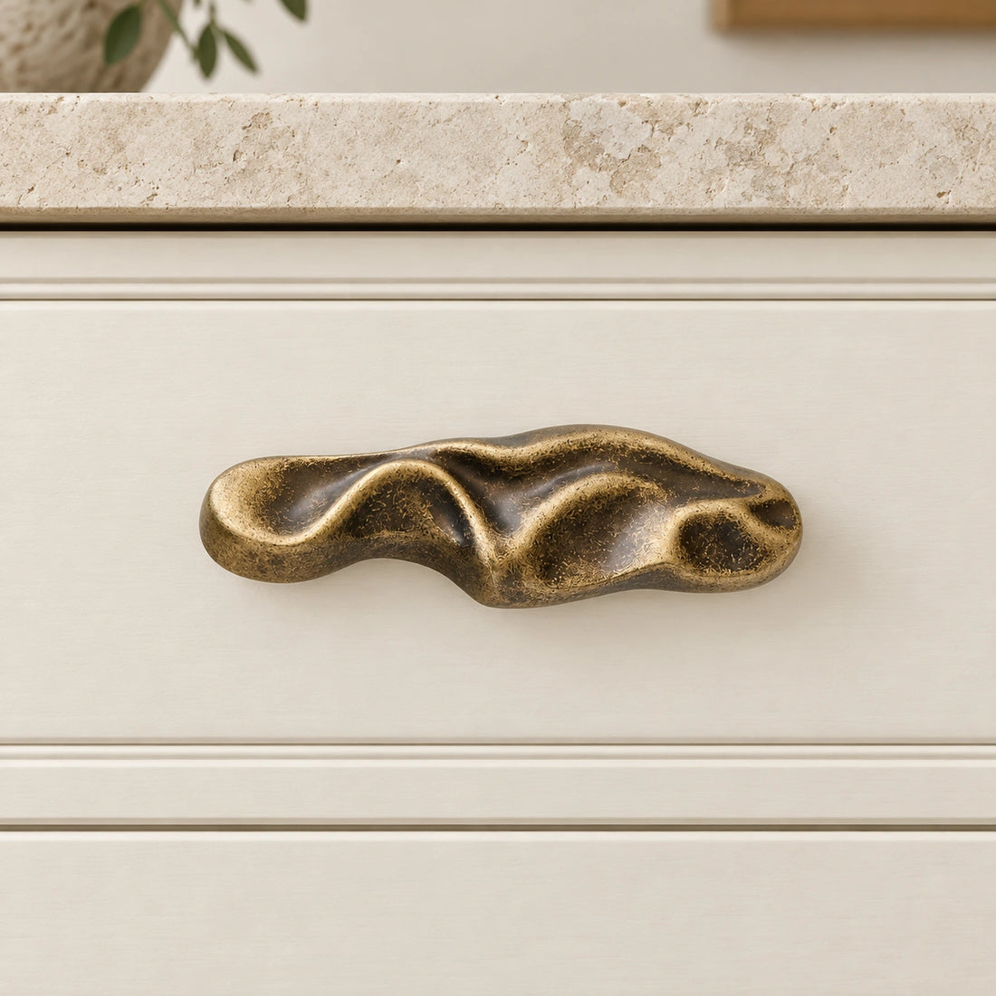 Aged and brushed antique brass sculptural wave cabinet pulls on pale limestone