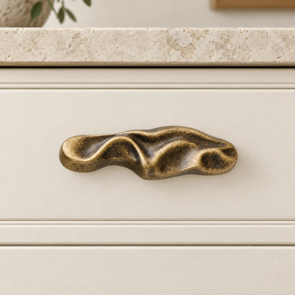 Aged antique brass wave pull mounted horizontally on an ivory drawer