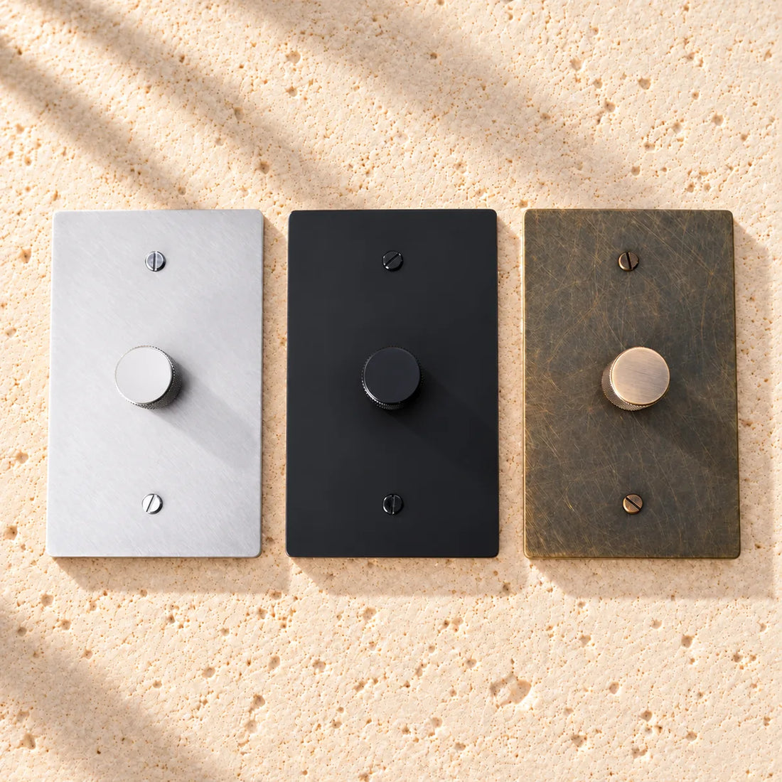 Fan speed control wall plates in stainless steel, matte black and aged bronze, mounted on sunlit limestone