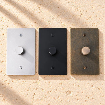 Fan speed control wall plates in stainless steel, matte black and aged bronze, mounted on sunlit limestone