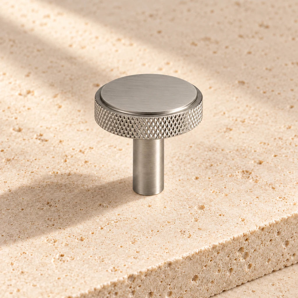 brushed nickel knurled round knob on pale limestone.