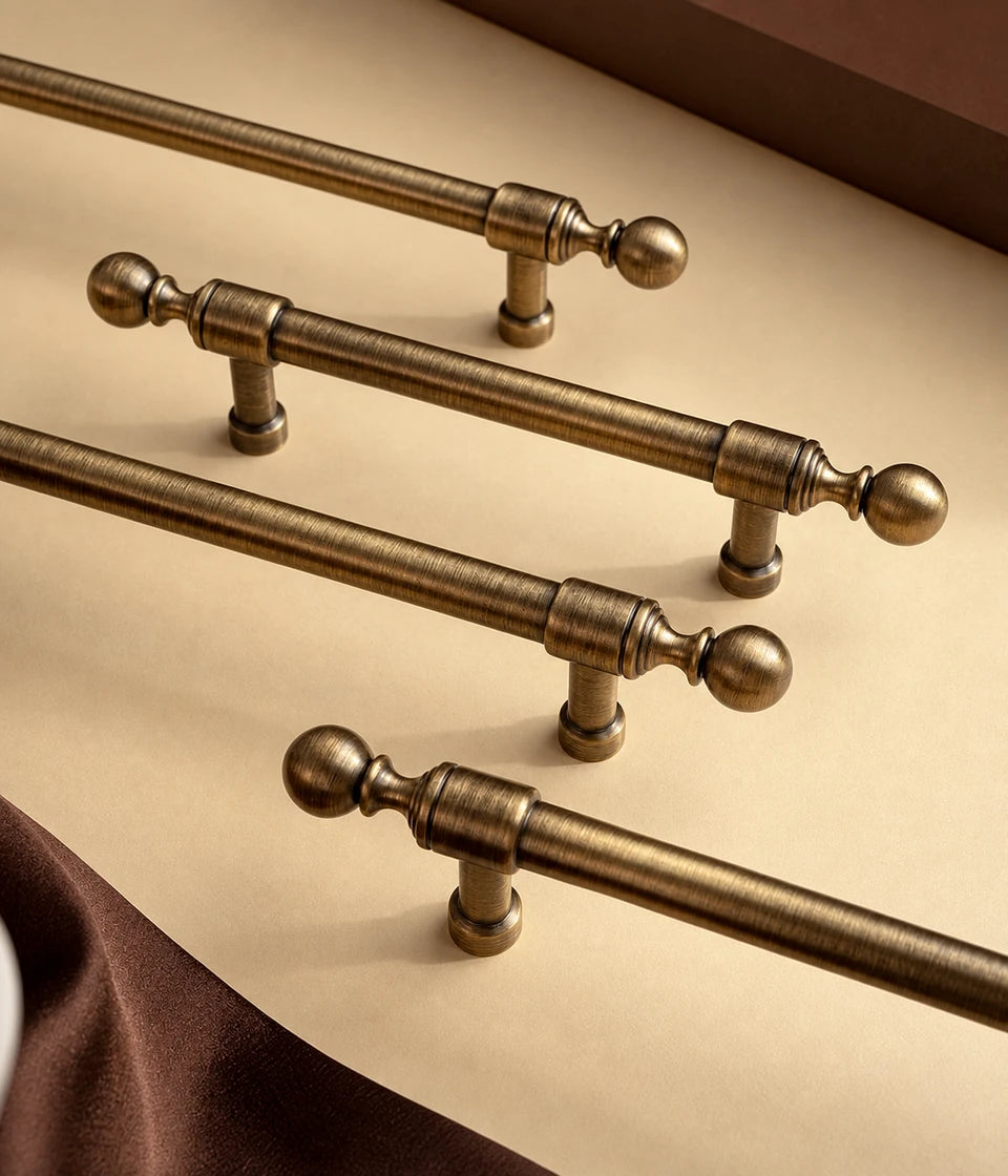 Straight antique brass cabinet pulls with turned ball ends arranged on a tabletop
