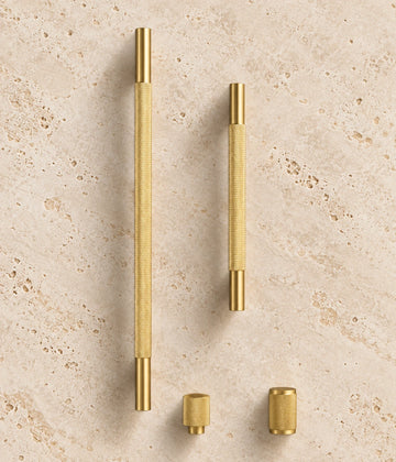 Cross-Knurled Brass Cabinet Pulls & Knobs arranged on warm limestone