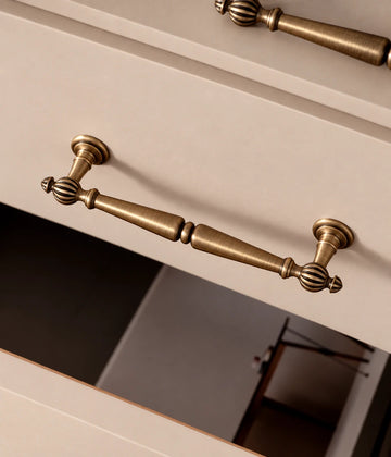 Antique brass cabinet pull with fluted ball finials and a double-tapered grip on a drawer