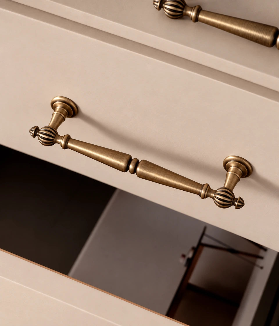 Antique brass cabinet pull with fluted ball finials and a double-tapered grip on a drawer
