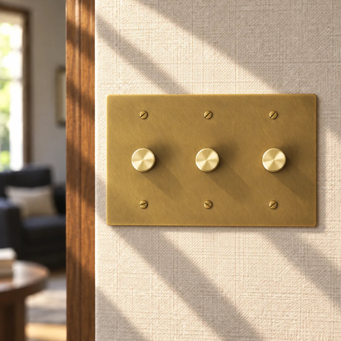 3-gang antique brass rotary dimmer switch with 3 matching knurled knobs and slotted screws, installed on a warm cream textured wall in natural sunlight.