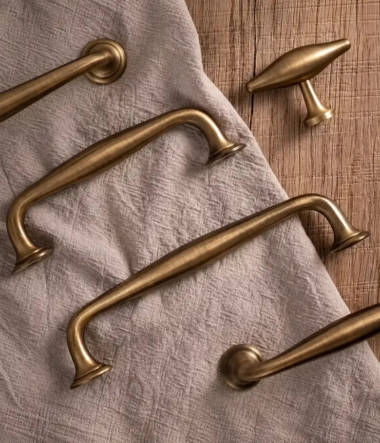 Solid brass arched cabinet pulls and oval T-knob in antique brushed brass on natural linen and wood