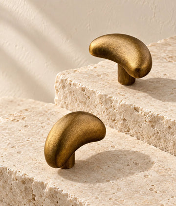 Antique brass crescent cabinet knobs arranged on ivory limestone