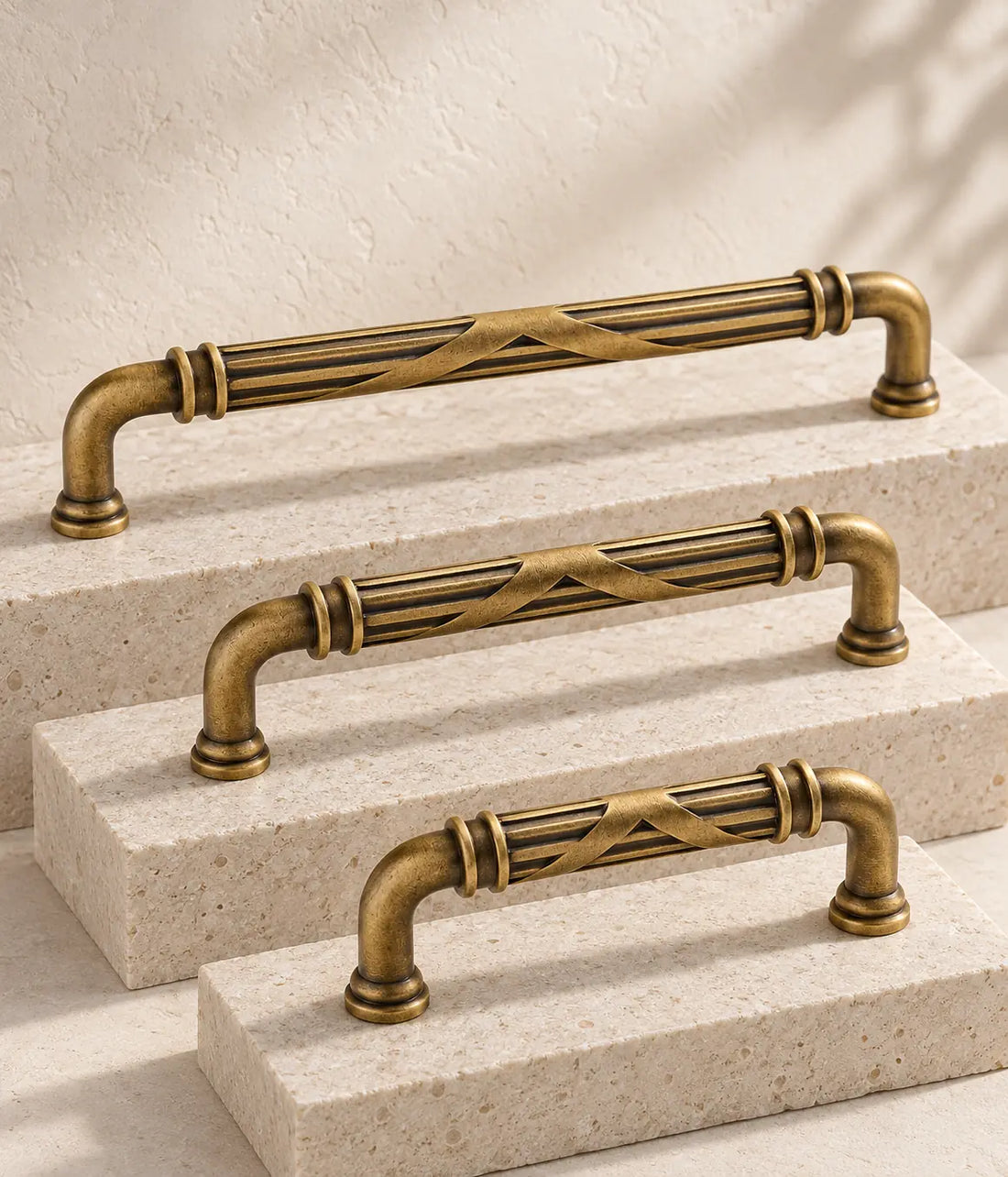 Antique brass cross-ribbon cabinet pulls in three sizes on ivory limestone