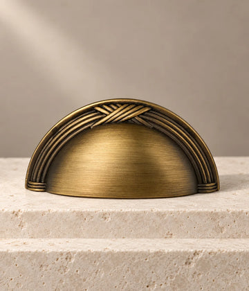 Antique brass cup pull with crossed-reed arched border on ivory limestone