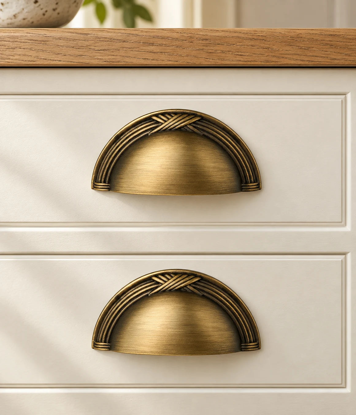 Decorative antique brass cup pulls installed on cream furniture drawers