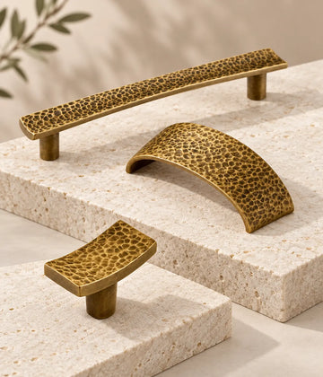 Antique brass hammered knob, broad arched pull and slim cabinet pull on ivory limestone