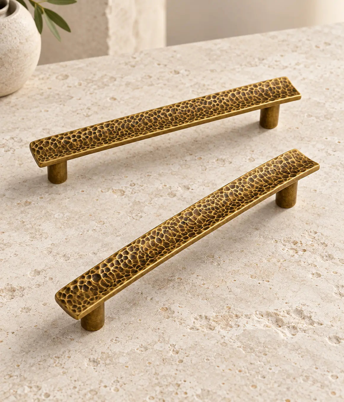 Slim hammered antique brass cabinet pulls arranged on pale limestone